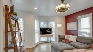Un salon avec un canapé gris, une échelle en bois, un bureau avec un téléviseur et un mur d’accent rouge.