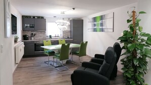 Une cuisine moderne avec des meubles gris, un plan de travail blanc et un coin repas comprenant une table blanche et des chaises vertes.