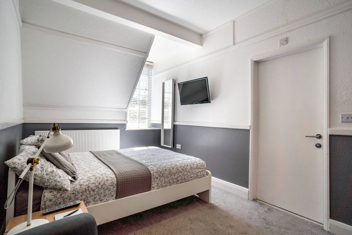 A bedroom with a bed, bedside table, lamp, and a TV mounted on the wall.