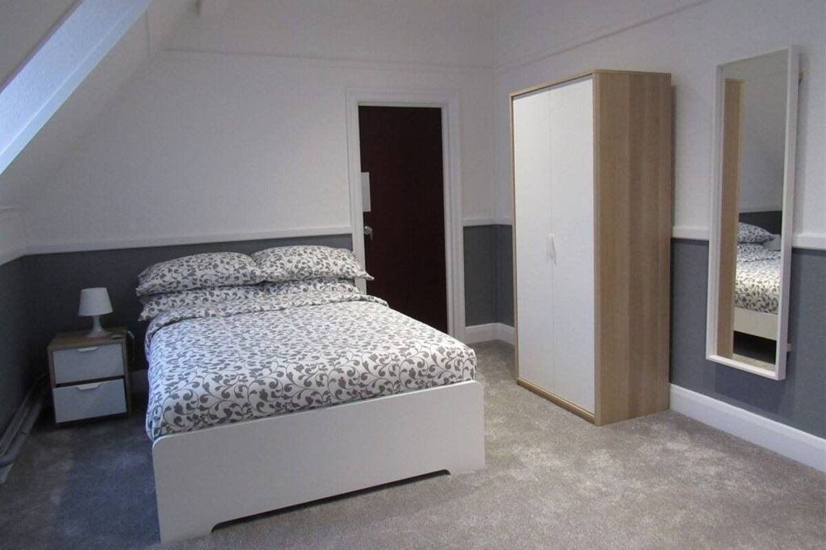 A bedroom with a bed, a wardrobe, a nightstand, and a mirror.