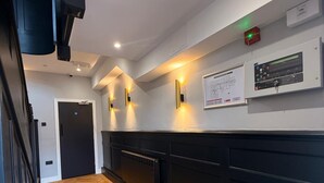 A hallway with a wooden herringbone floor, black carpet, and a black wall with a control panel and a framed diagram.