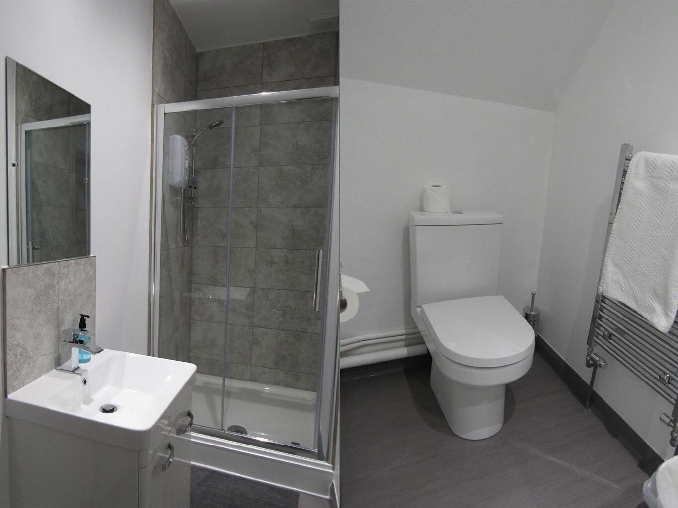 A bathroom with a shower, toilet, sink, and towel rack.