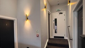 A hotel hallway with carpeted stairs, wall-mounted lighting, and a door with an emergency exit sign.