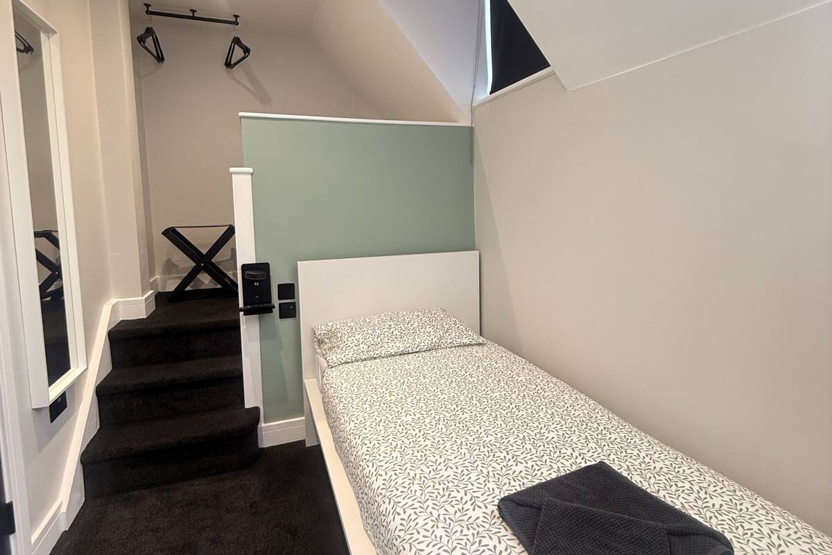 A compact bedroom with a single bed, a small desk, and a staircase leading to an upper level.