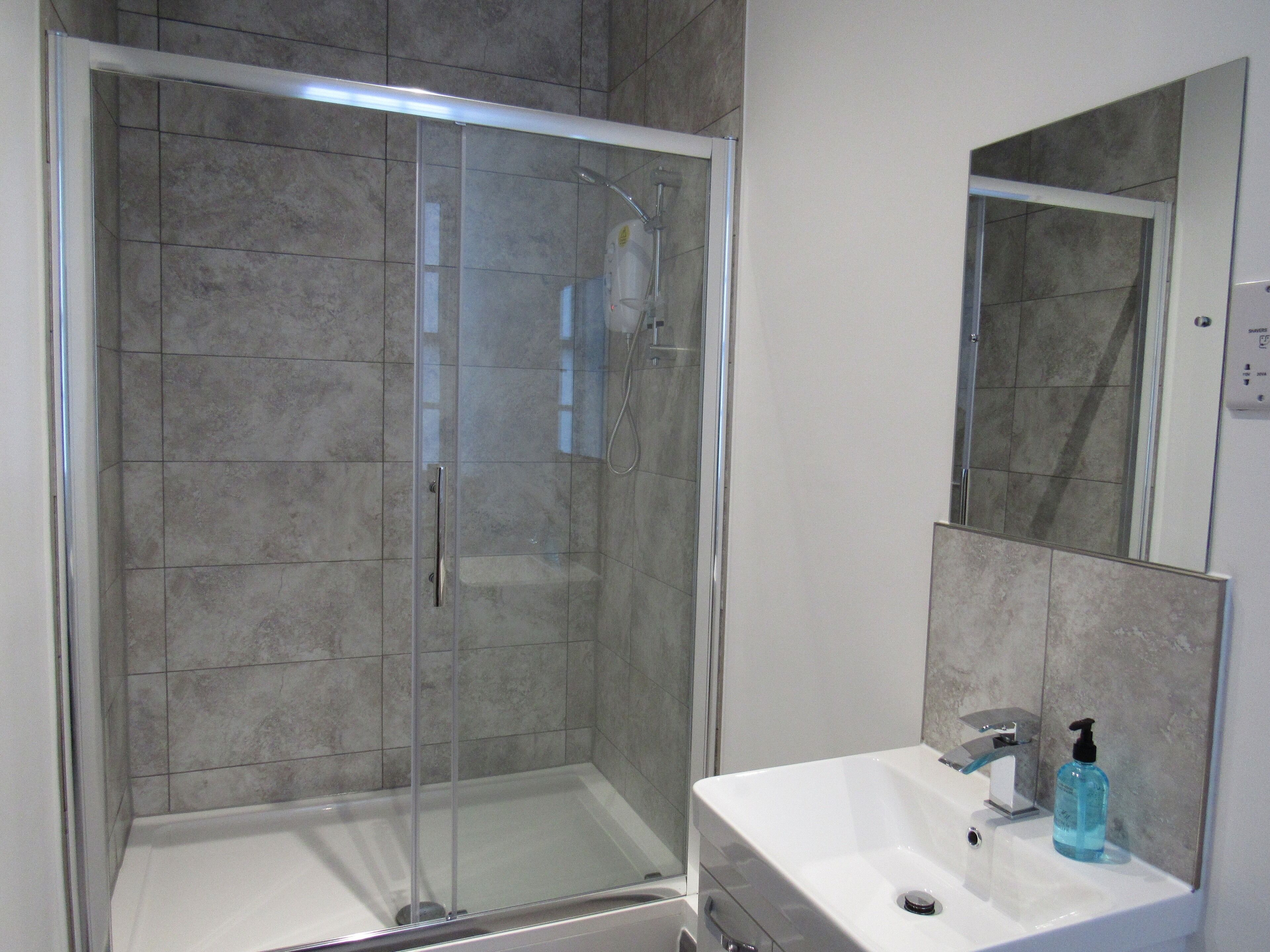 A modern bathroom with a glass-enclosed shower, a white sink, and a mirror above it.