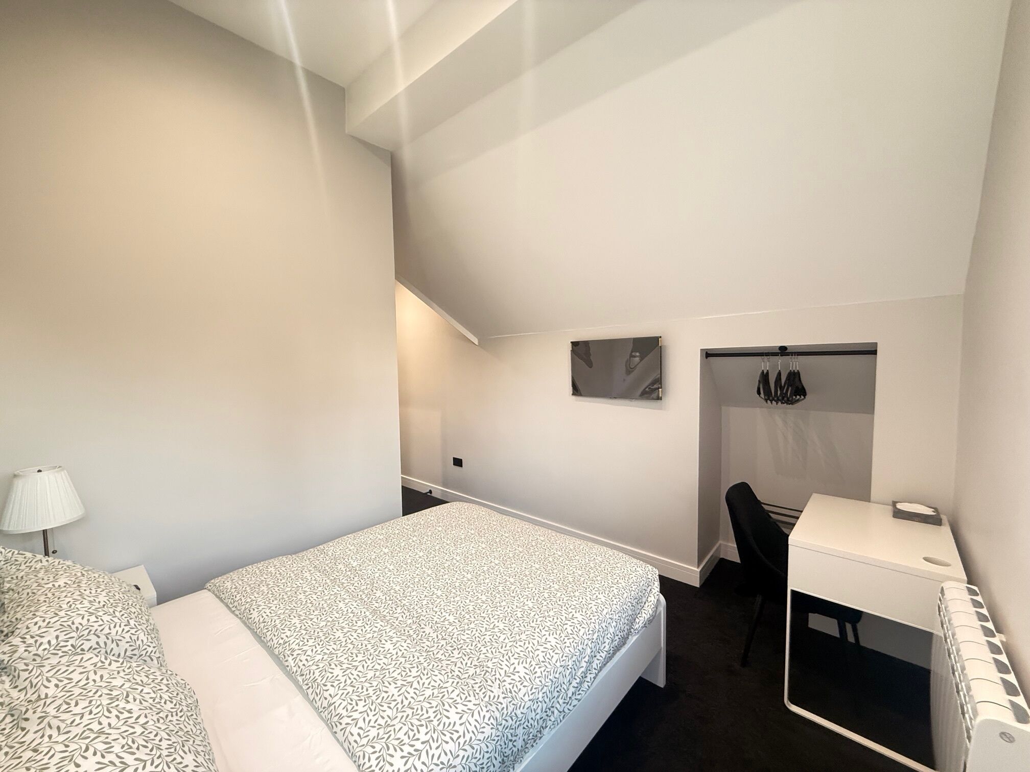 A modern hotel room with a bed, a desk, and a chair.