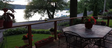 A wooden deck with a table and chairs, overlooking a lake with boats and a dock.