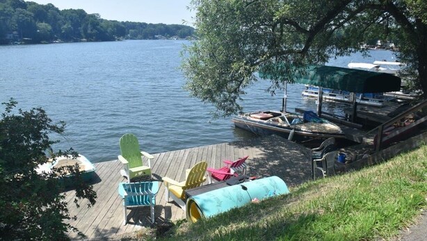 Un molo sul lago con sedie Adirondack colorate, un tavolo da picnic coperto e una barca ormeggiata nelle vicinanze.