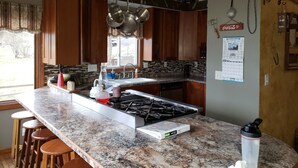 Cucina con piano di lavoro in granito, mobili in legno, fornello a gas e una finestra che lascia entrare luce naturale.
