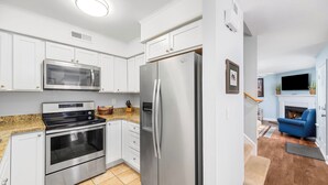 A modern kitchen with white cabinets, stainless steel appliances, and a blue sofa in the adjacent living area.