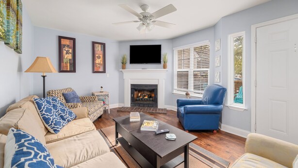 A living room with a sofa, armchair, coffee table, fireplace, television, and a ceiling fan.