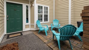 A house exterior with a green door, beige siding, a window, and outdoor seating with chairs and a table.