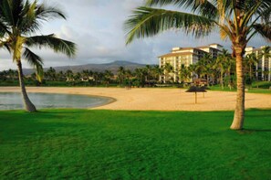 A beachfront hotel with palm trees, a sandy beach, and a view of mountains in the background.