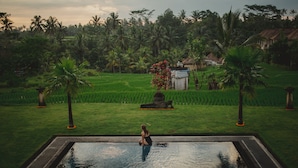 A woman sitting by a pool with a view of a lush garden and a traditional house in the background. - B Saya Villas Ubud (Ubud)