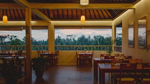A restaurant with wooden tables and chairs, potted plants, and large windows overlooking a tropical landscape. - B Saya Villas Ubud (Ubud)