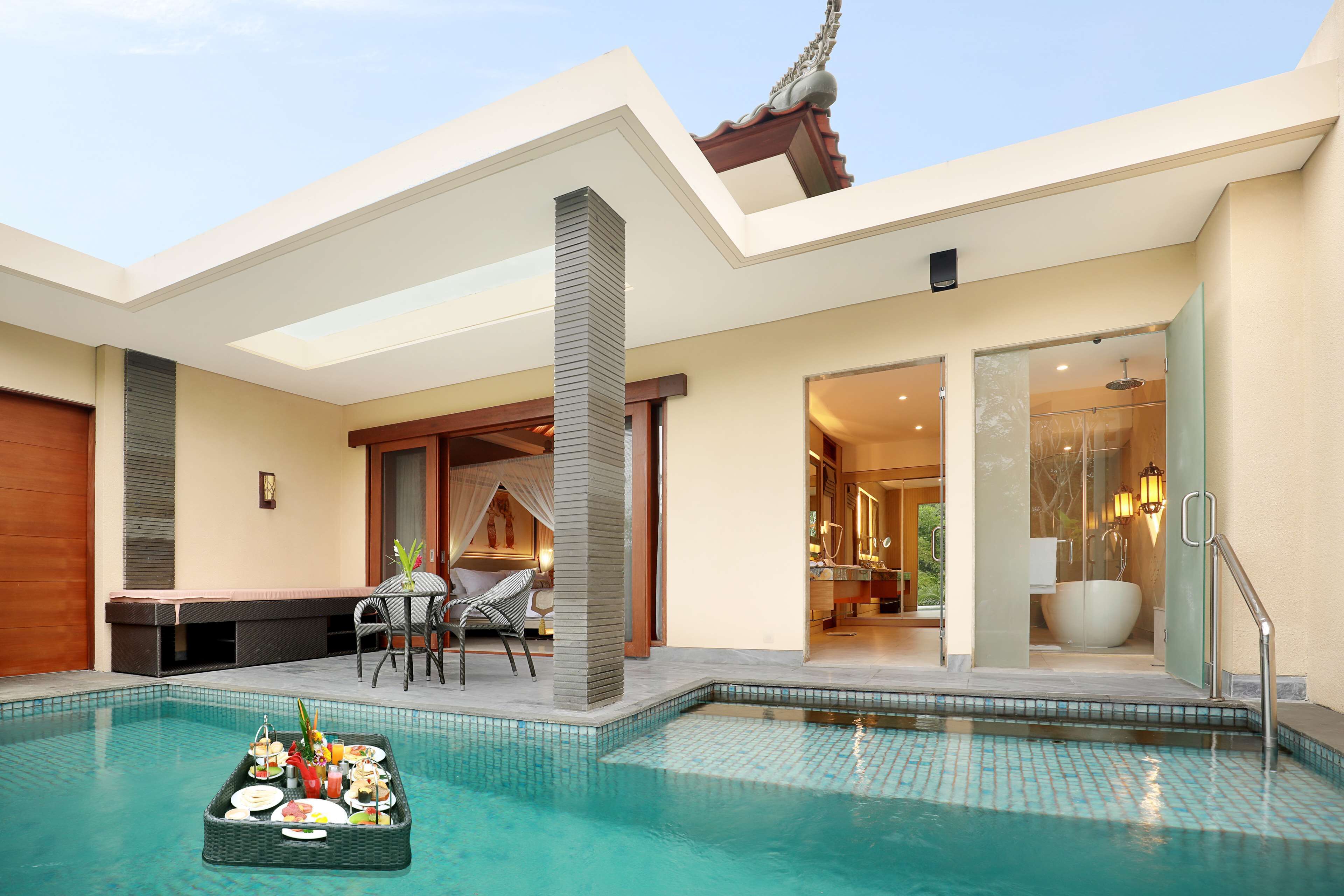 A modern pool area with a dining setup and a glass-enclosed bathroom.