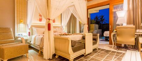 A well-lit bedroom with a canopy bed, a sitting area with a chair, a desk, and a view of the outdoors.