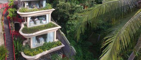 Un edificio de varios niveles con balcones, rodeado de abundante vegetación y palmeras.