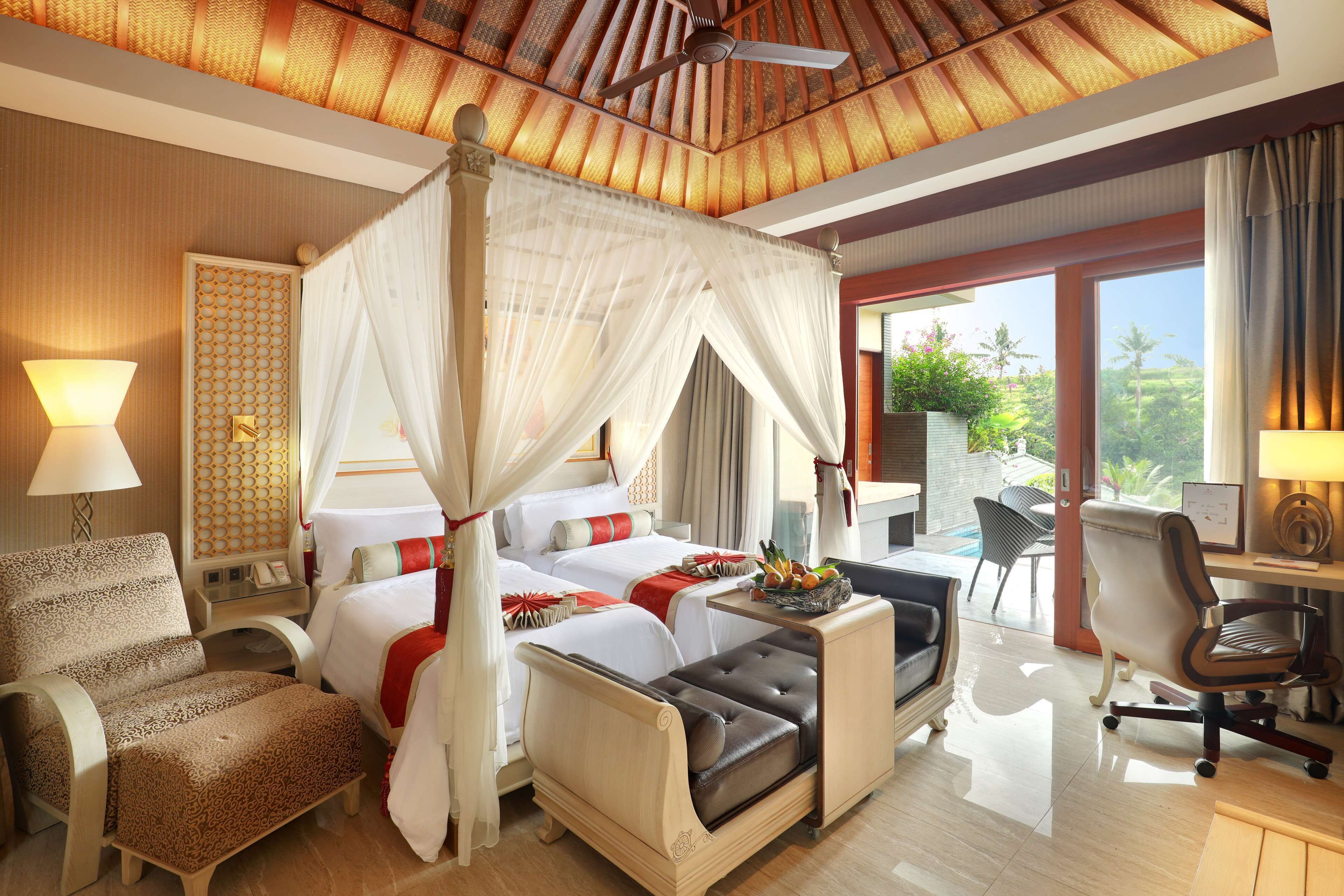 A spacious bedroom with a canopy bed, a sitting area with a desk, and a view of the outdoors.