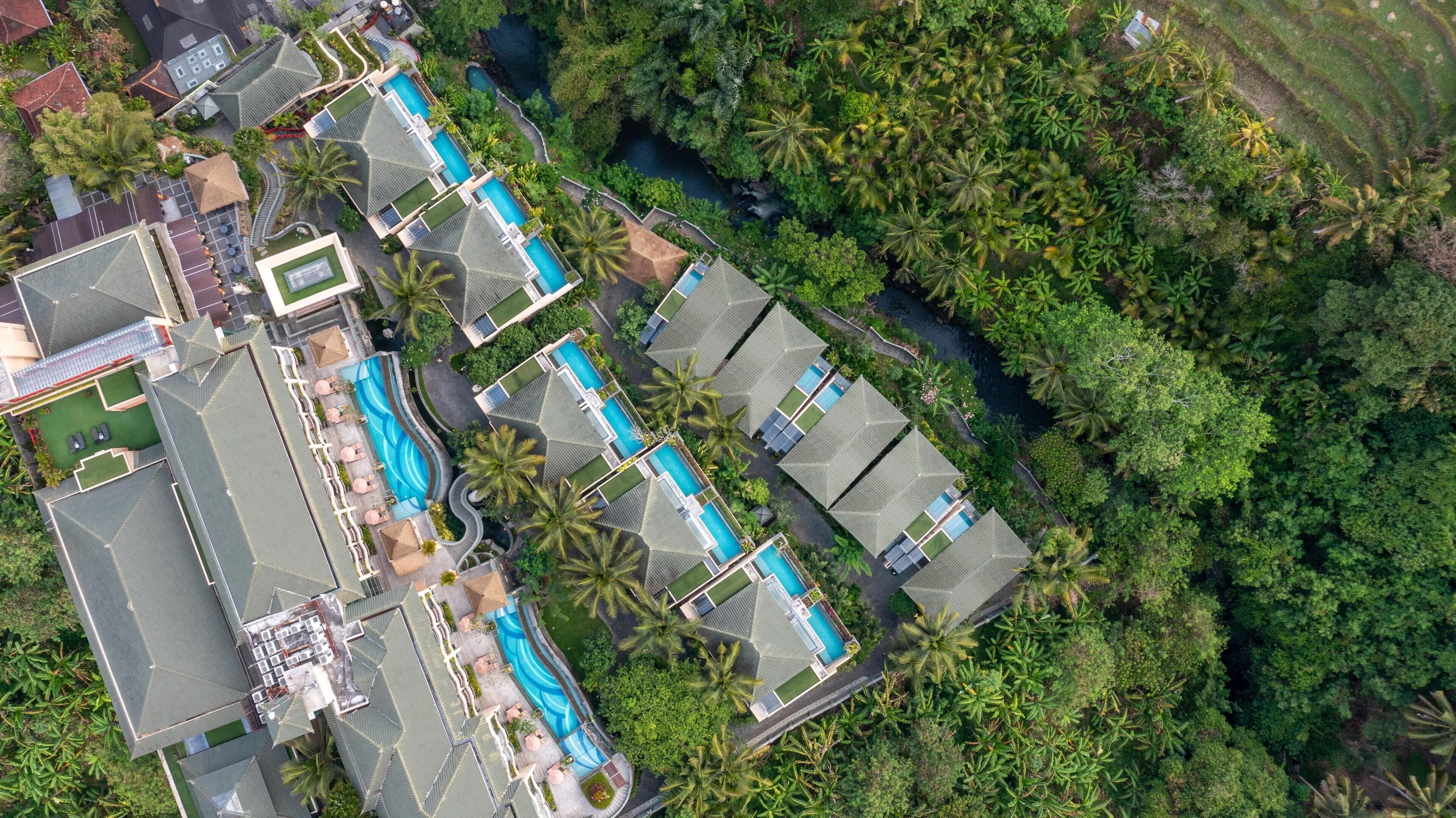 Luftaufnahme eines Resorts mit mehreren Schwimmbecken, Palmen und einem Fluss.