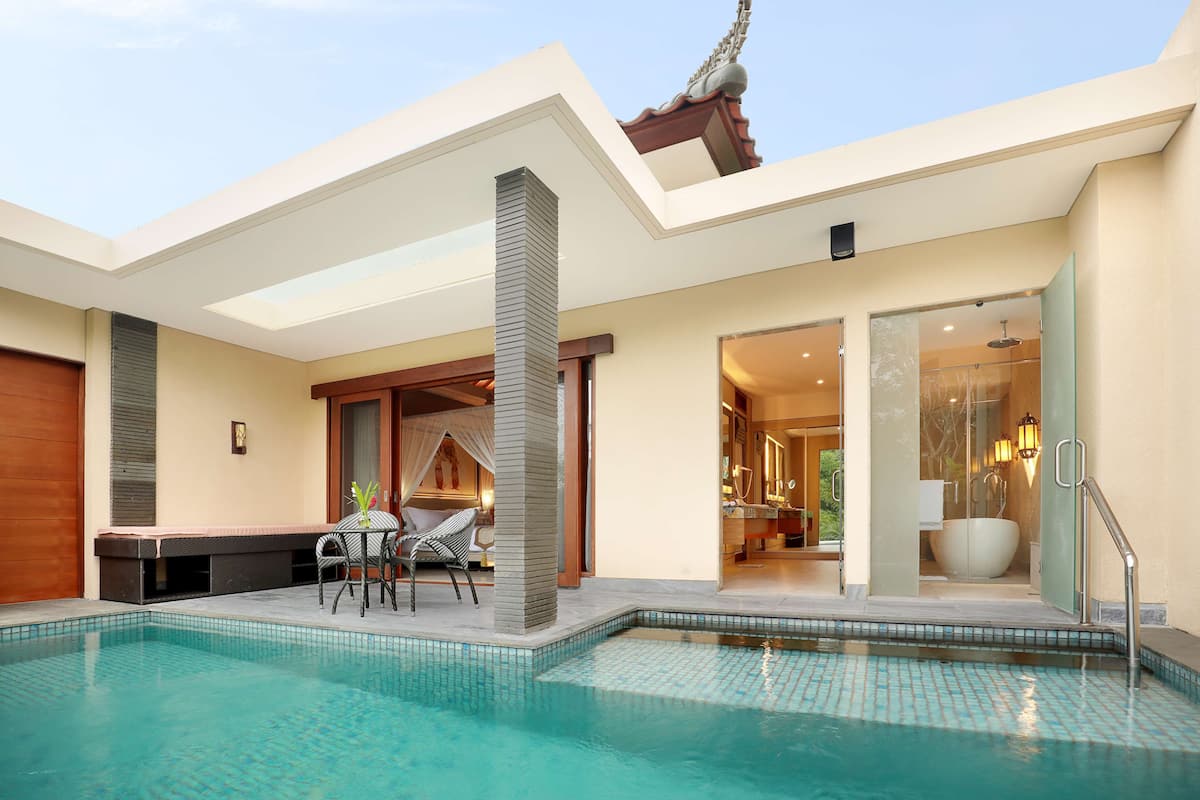 A modern pool area with a clear view of the pool, a seating area with chairs, and a glass-enclosed bathroom with a bathtub.
