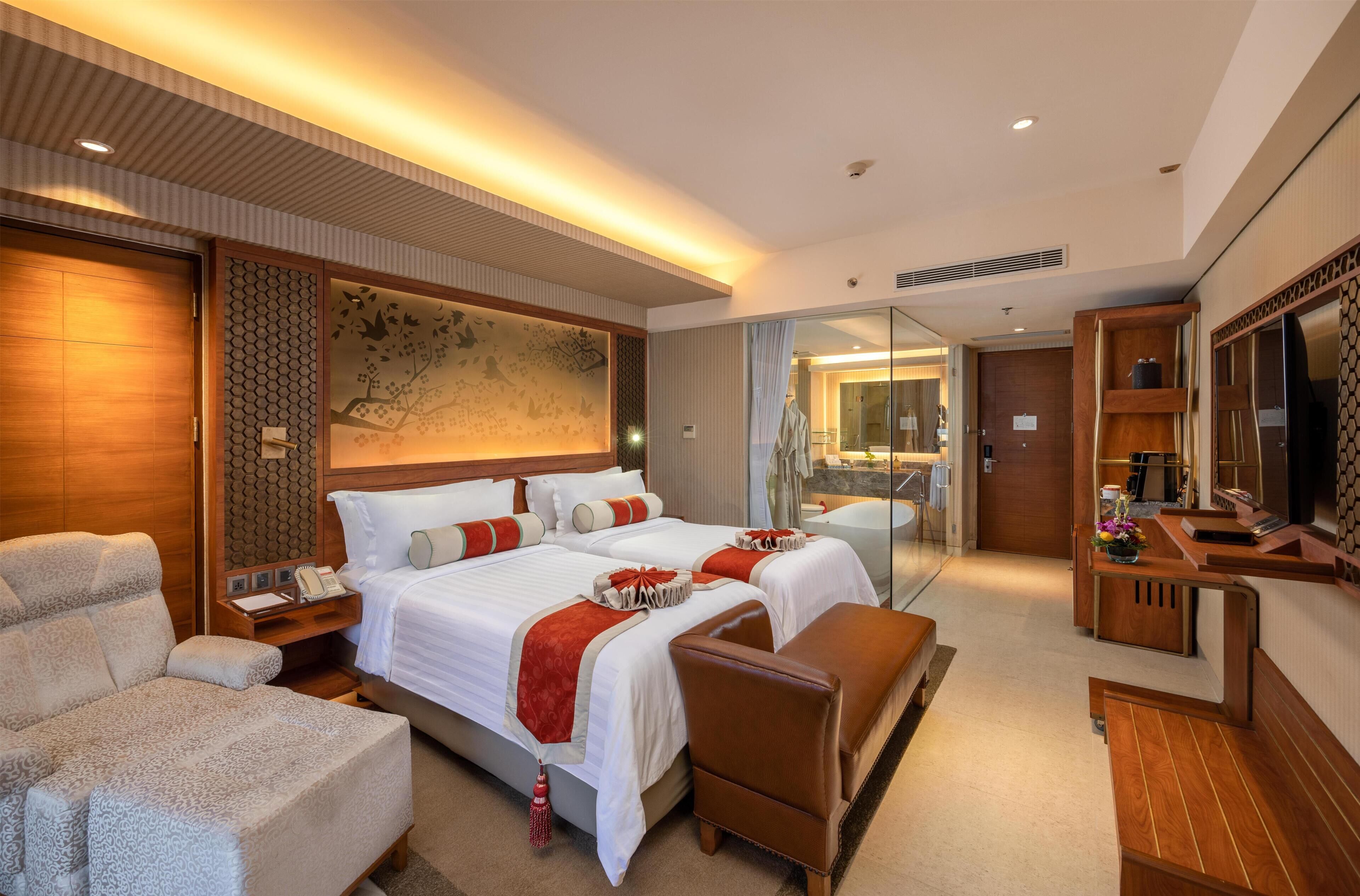 A hotel room with two beds, a sofa, a desk, a mirror, and a television.