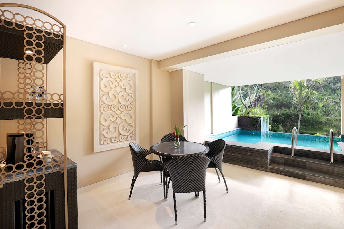 A modern indoor pool area with a round table and chairs, a decorative wall panel, and a view of the outdoor pool.