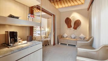 Una habitación de hotel moderna con cocina, zona de estar con sofá y sillones, y un elemento decorativo en la pared.