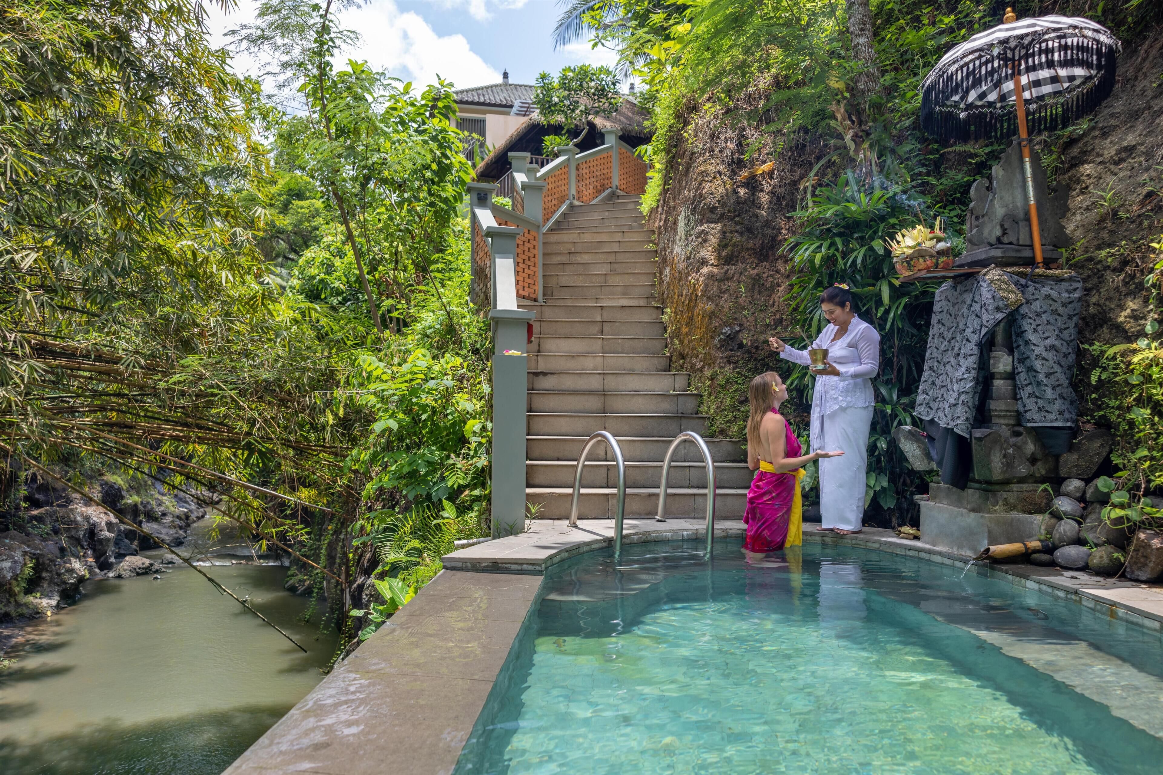 A pool area with a staircase leading to a building, surrounded by lush greenery.
