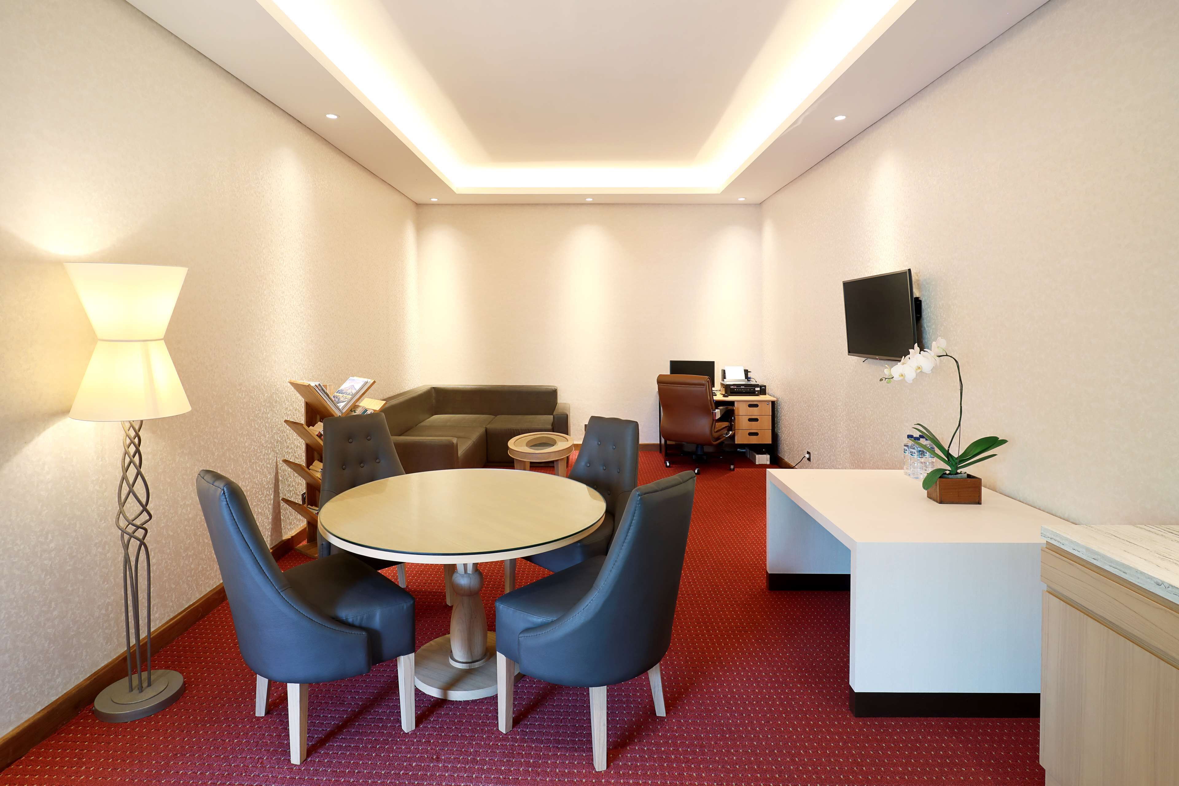 Une chambre d’hôtel avec une table ronde, quatre chaises, un canapé, une télévision, un bureau et une lampe.