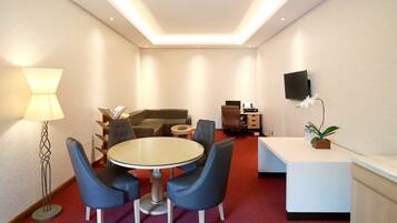 Une chambre d’hôtel avec une table ronde, quatre chaises, un canapé, une télévision, un bureau et une lampe.