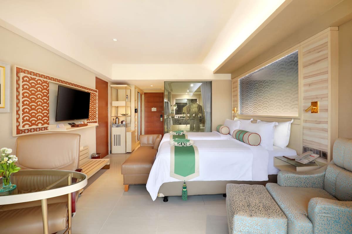A hotel room with a large bed, a TV, a seating area with a table, and a view of the bathroom.
