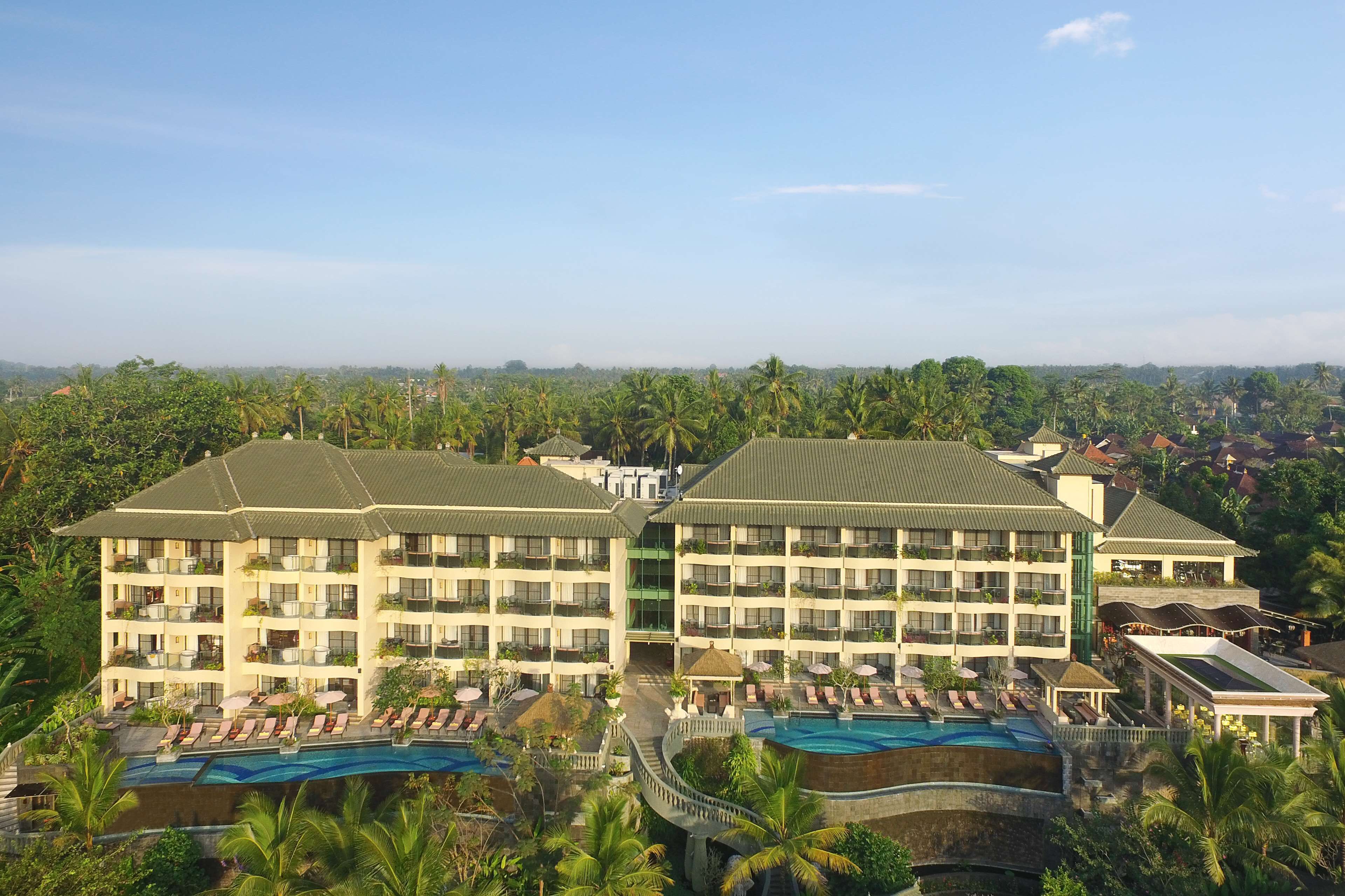 Un hotel de varios pisos, una piscina y exuberante vegetación a su alrededor.