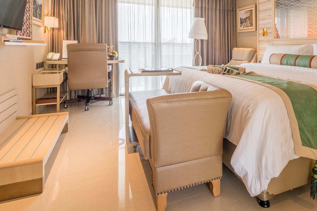 A hotel room with a bed, a desk, a chair, a TV, and a window with curtains.
