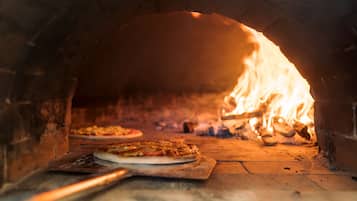 En murstense ovn med to pizzaer indeni, flammer synlige gennem åbningen.