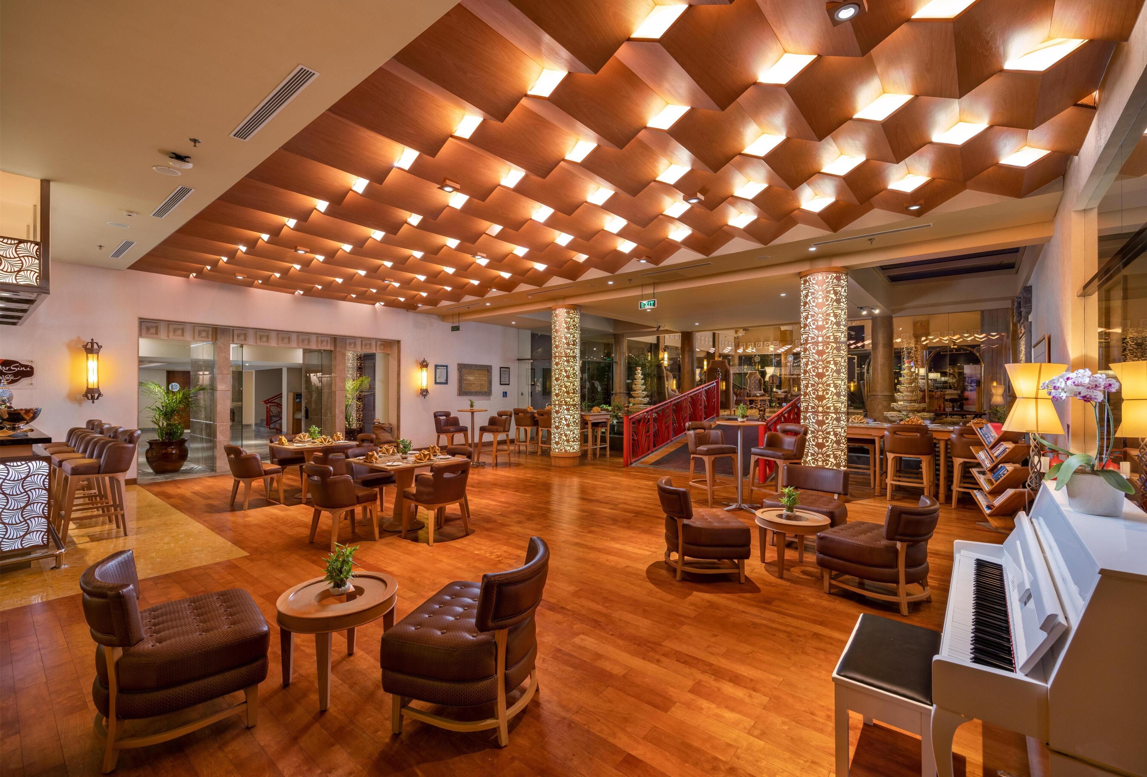 A spacious lobby with wooden flooring, multiple seating areas, a piano, and a staircase leading to upper floors.