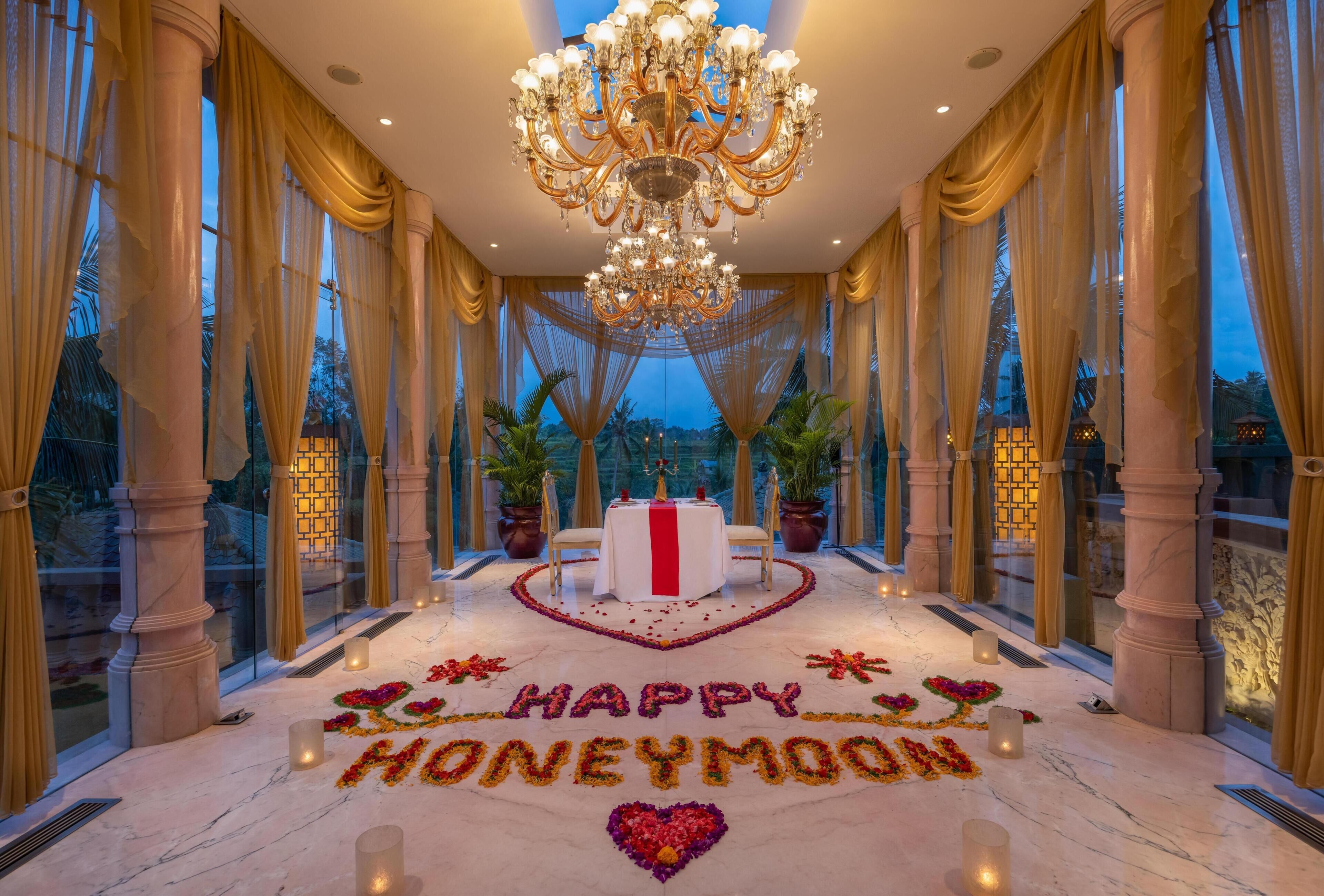 A luxurious room with a chandelier, large windows, and a table with a red centerpiece.