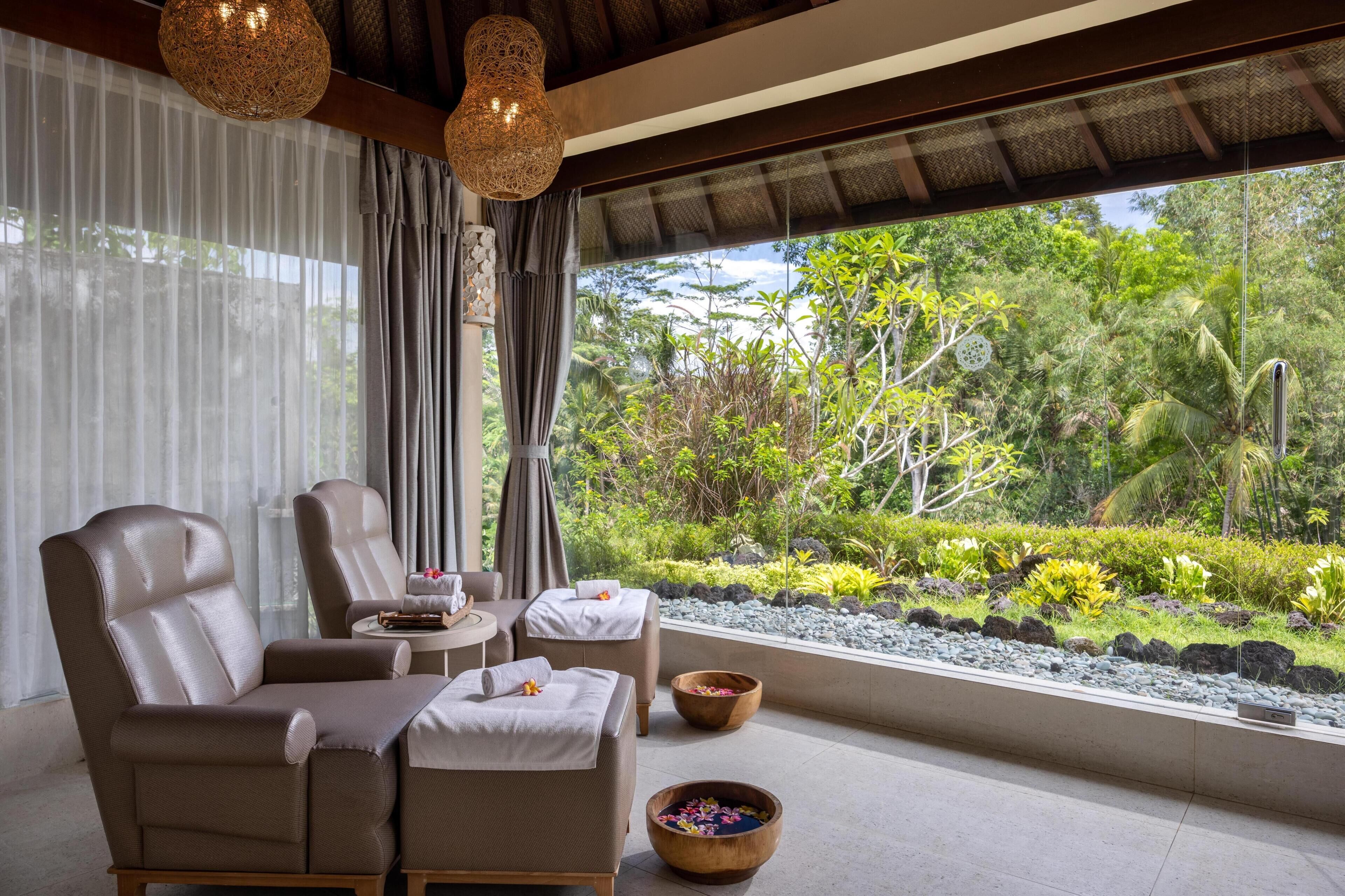 A room with two leather chairs, a small table, and a view of a lush garden through large windows.