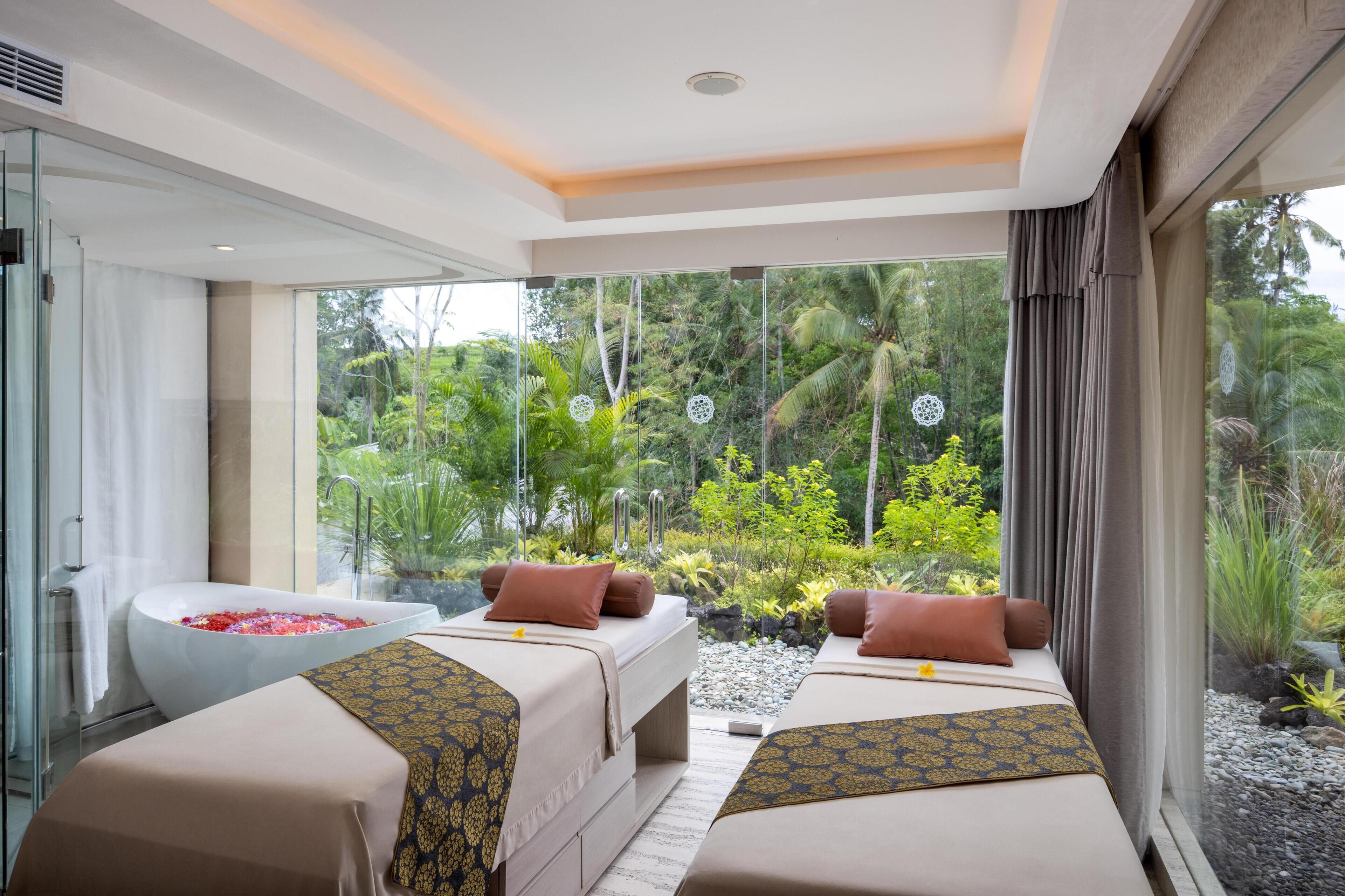 A modern room with a glass shower, two beds with patterned bedding, and a view of lush greenery.