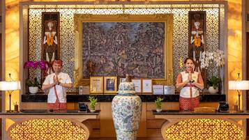 Uma área de recepção com um vaso grande, obras de arte emolduradas e uma caixa de atendimento ao hóspede.