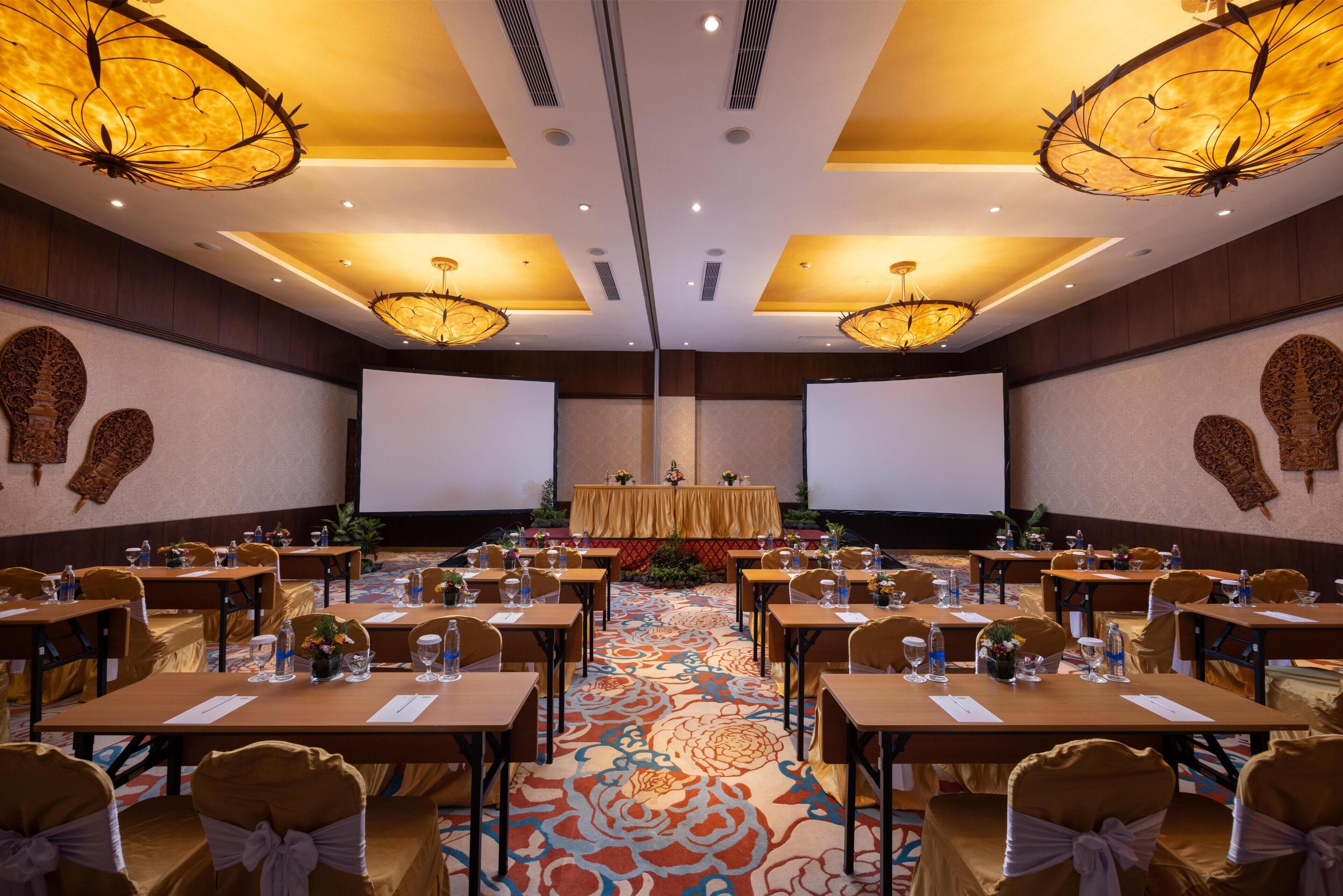 A conference room with tables, chairs, and a stage with a screen.