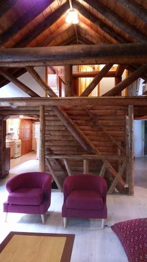 A spacious attic room with exposed wooden beams, a wooden staircase, and two purple armchairs.