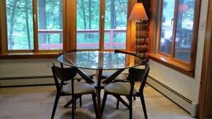 A round glass table with four chairs in a room with large windows overlooking a forest.