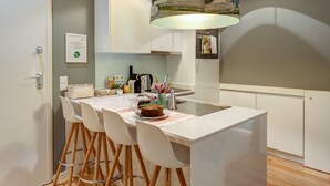 Een moderne keuken met een wit kookeiland, barkrukken en een hangende lamp.