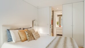Een slaapkamer met een bed, kussens, een nachtkastje en een kledingkast.