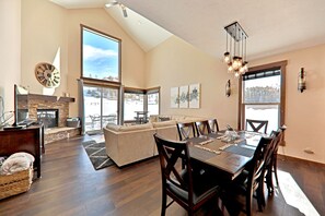 A spacious living area with a fireplace, a dining table with chairs, and a large window offering a view of a snowy landscape.