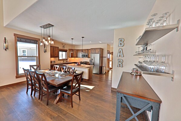 A modern kitchen with wooden cabinets, a central island, stainless steel appliances, and a dining area with a wooden table and chairs.