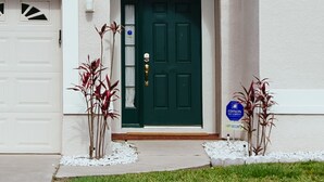 A two-story building with a green front door, white garage door, and a small porch area with plants. - EAGLE POINTE SOUTH ON THE LARGER LAKE  A NEW VACATION/HOLIDAY EXPERIENCE (Kissimmee)