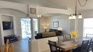 A modern living room with a TV, seating area, dining table, and a chandelier. - EAGLE POINTE SOUTH ON THE LARGER LAKE  A NEW VACATION/HOLIDAY EXPERIENCE (Kissimmee)