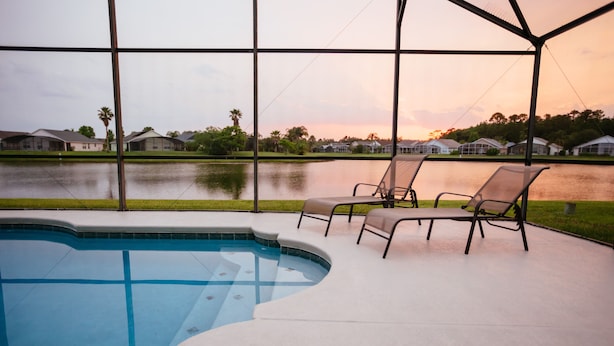 A swimming pool with lounge chairs and a view of houses across a body of water. - EAGLE POINTE SOUTH ON THE LARGER LAKE  A NEW VACATION/HOLIDAY EXPERIENCE (Kissimmee)